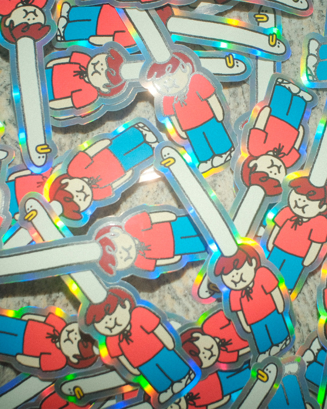 Holographic stickers of a character with a a red shirt and blue pants, wearing a comically long goose-shaped hat, on a reflective surface.